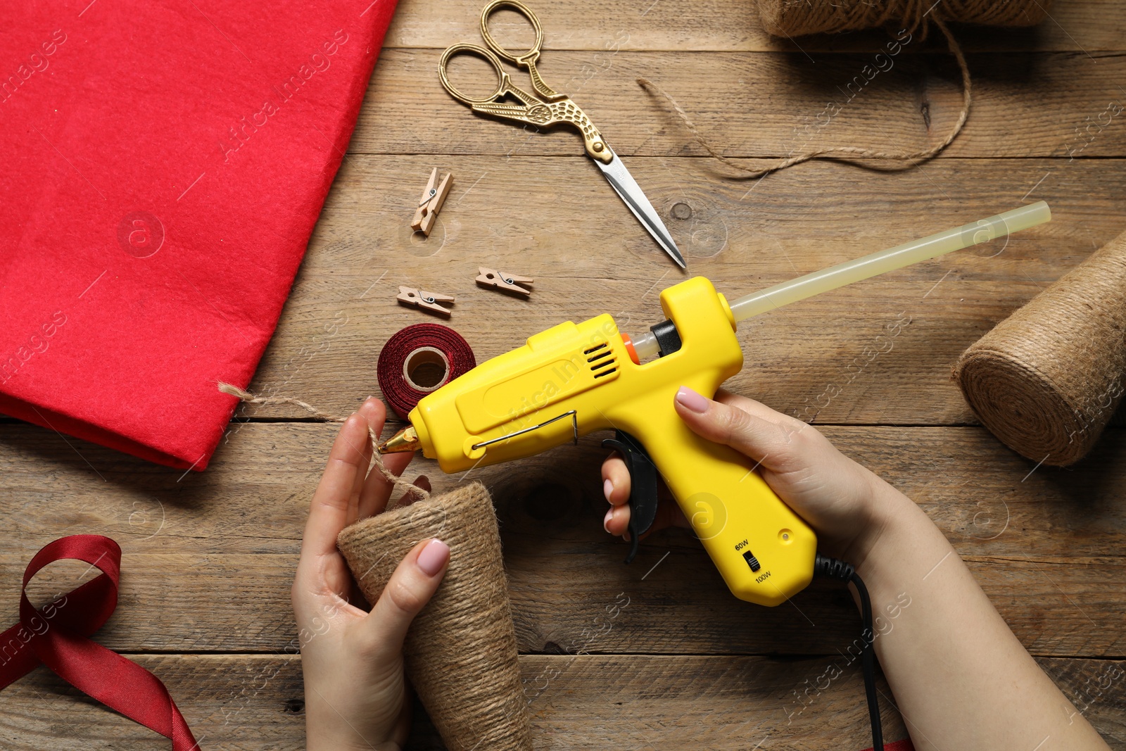 Photo of Woman with hot glue gun making craft at wooden table, top view