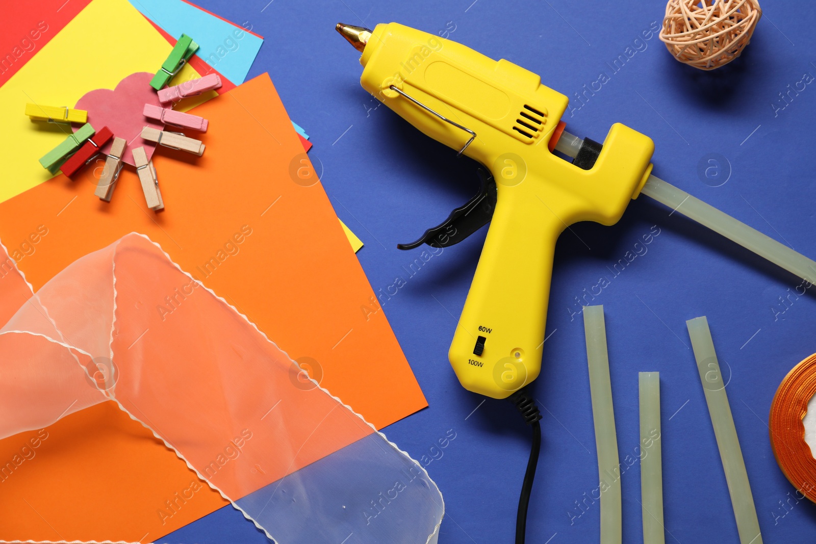 Photo of Hot glue gun and handicraft materials on blue background, flat lay