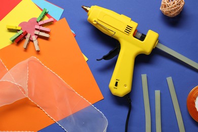 Photo of Hot glue gun and handicraft materials on blue background, flat lay