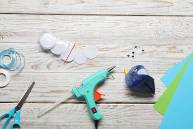 Photo of Hot glue gun and handicraft materials on white wooden table, flat lay