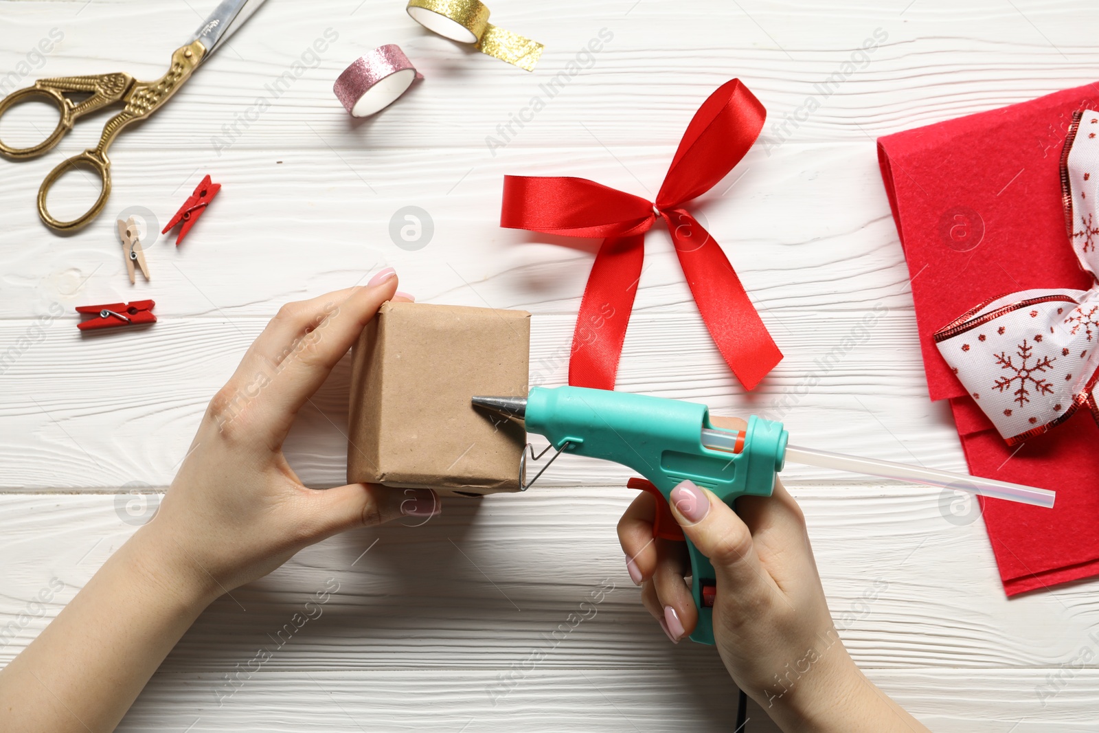 Photo of Woman with hot glue gun making craft at white wooden table, top view