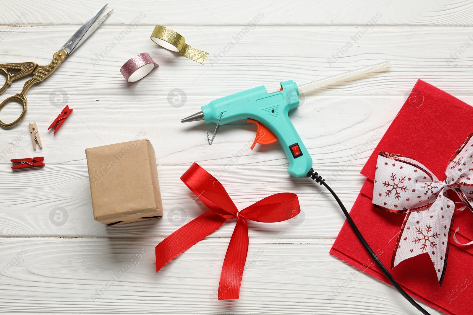 Photo of Hot glue gun and handicraft materials on white wooden table, flat lay