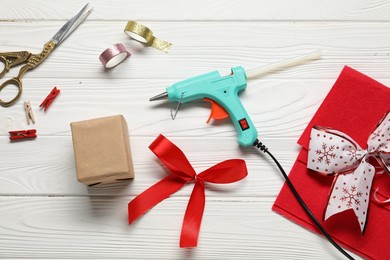 Photo of Hot glue gun and handicraft materials on white wooden table, flat lay