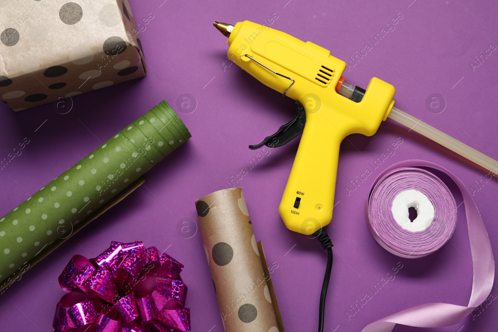 Photo of Hot glue gun and handicraft materials on purple background, flat lay