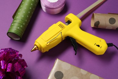 Photo of Hot glue gun and handicraft materials on purple background, closeup