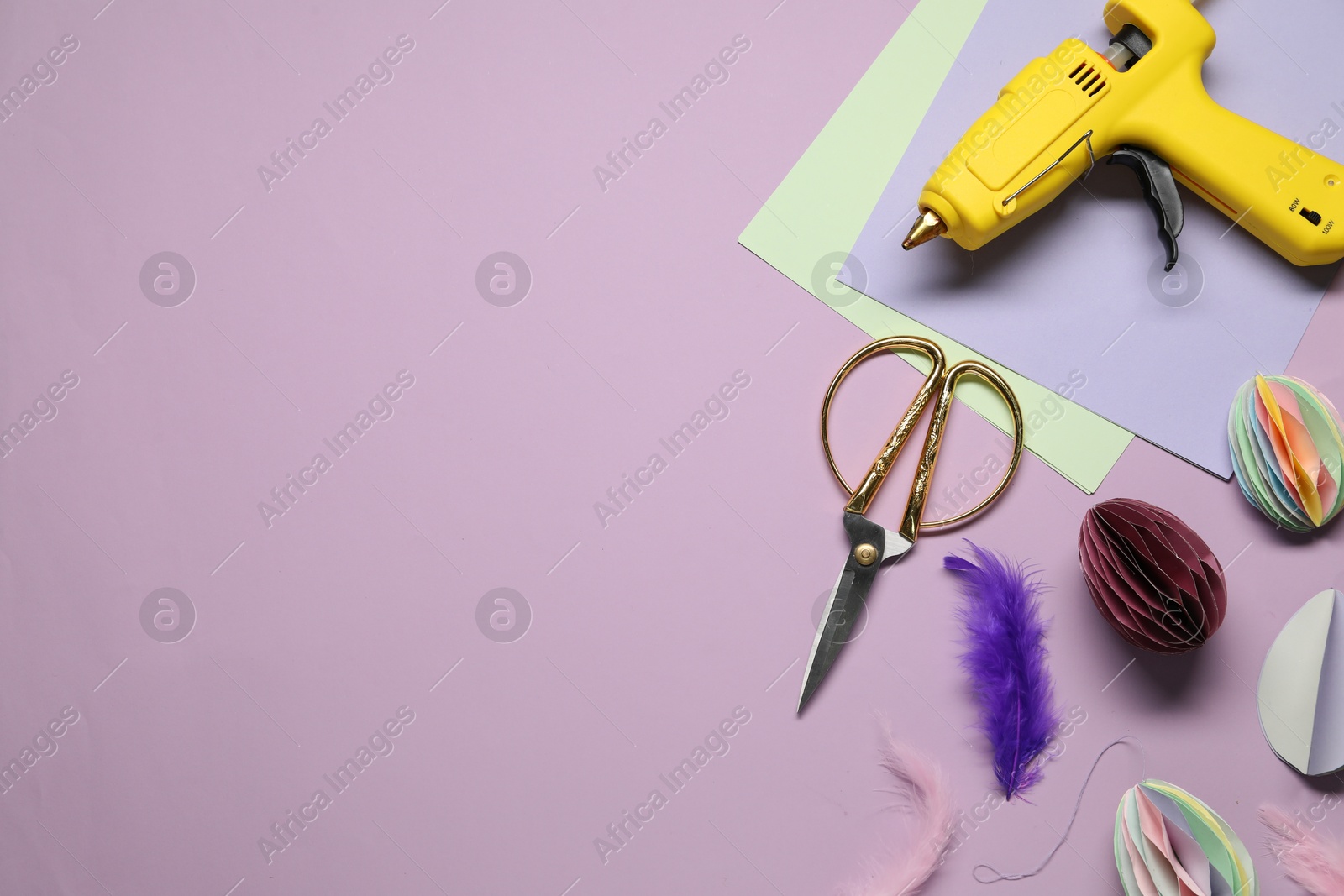 Photo of Hot glue gun and handicraft materials on violet background, flat lay. Space for text