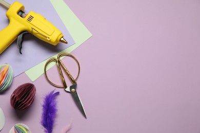 Photo of Hot glue gun and handicraft materials on violet background, flat lay. Space for text