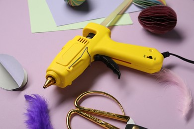 Photo of Hot glue gun and handicraft materials on violet background, closeup