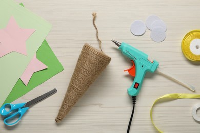 Photo of Hot glue gun and handicraft materials on white wooden table, flat lay