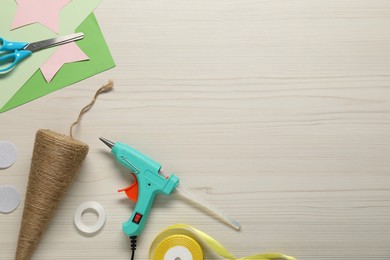 Photo of Hot glue gun and handicraft materials on white wooden table, flat lay. Space for text