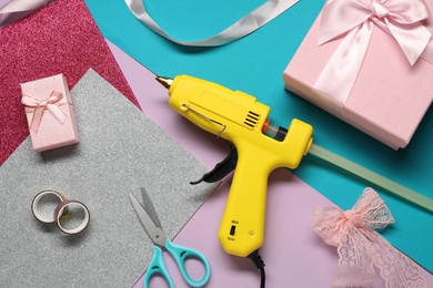 Photo of Hot glue gun, gift boxes and handicraft materials on color background, flat lay