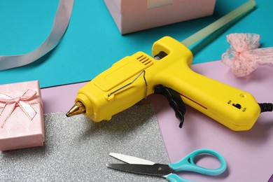 Photo of Hot glue gun, gift box and handicraft materials on color background, closeup