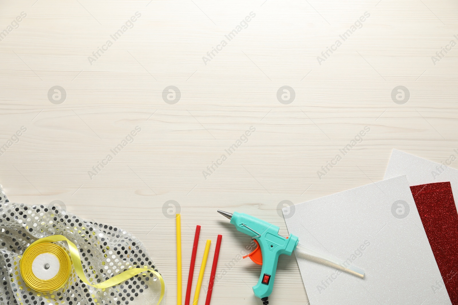 Photo of Hot glue gun and handicraft materials on white wooden table, flat lay. Space for text