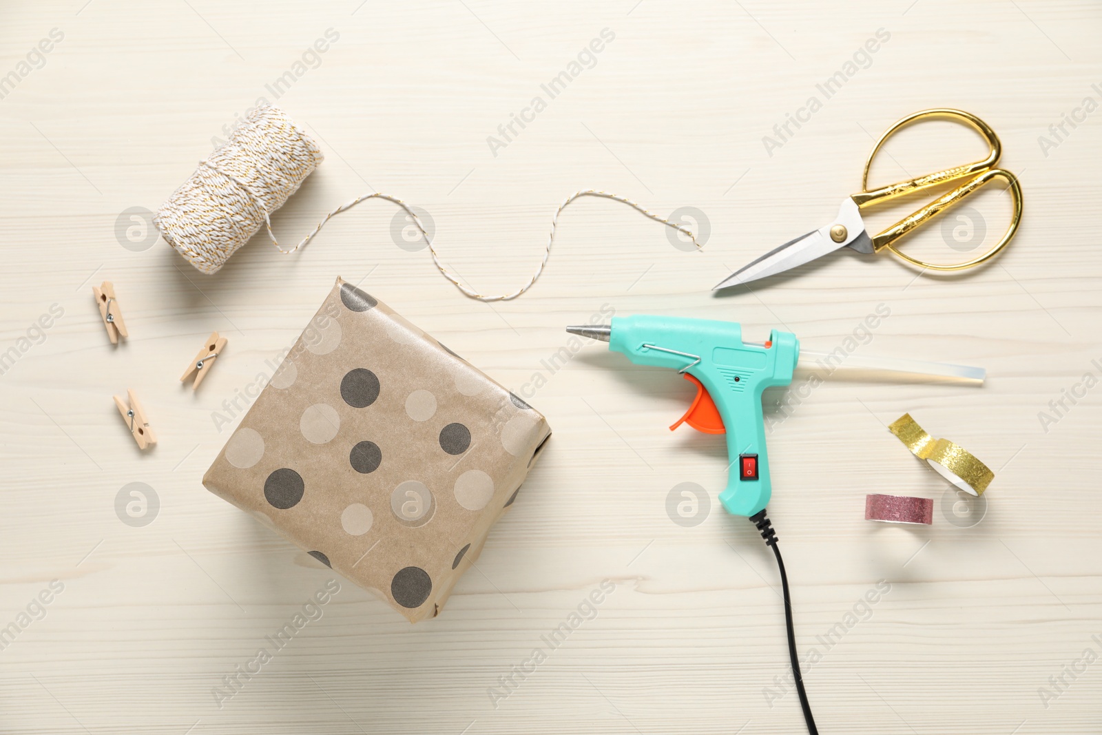 Photo of Hot glue gun and handicraft materials on white wooden table, flat lay