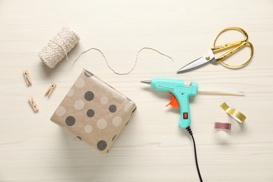 Photo of Hot glue gun and handicraft materials on white wooden table, flat lay