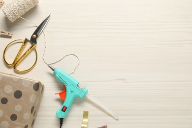 Photo of Hot glue gun and handicraft materials on white wooden table, flat lay. Space for text