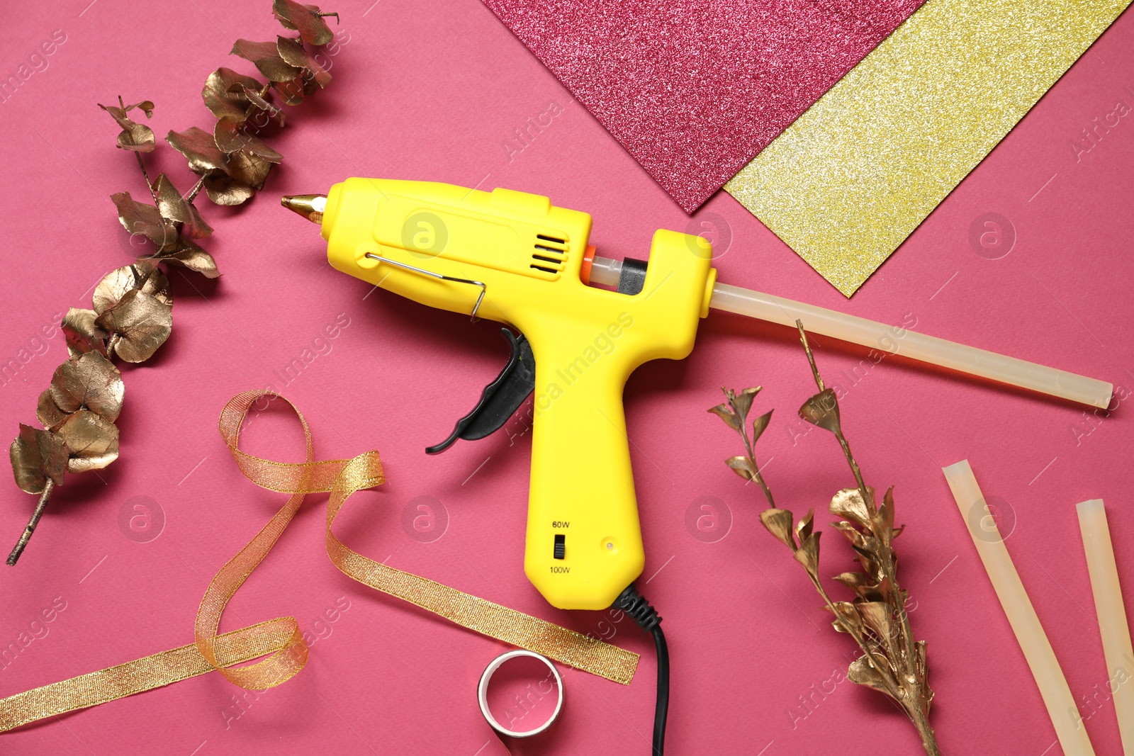 Photo of Hot glue gun and handicraft materials on crimson background, flat lay