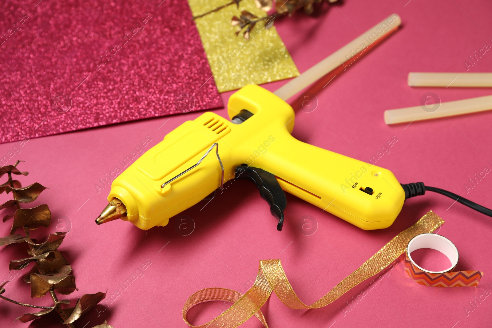 Photo of Hot glue gun and handicraft materials on crimson background, closeup