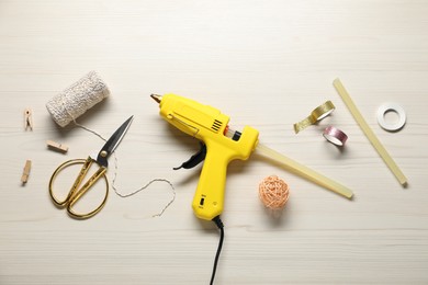 Photo of Hot glue gun and handicraft materials on white wooden table, flat lay