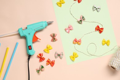 Photo of Hot glue gun and handicraft materials on pink background, flat lay