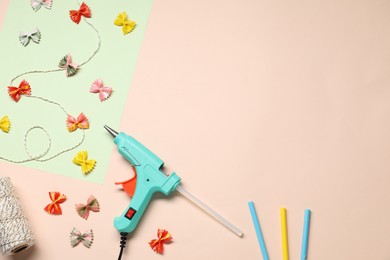 Photo of Hot glue gun and handicraft materials on pink background, flat lay. Space for text