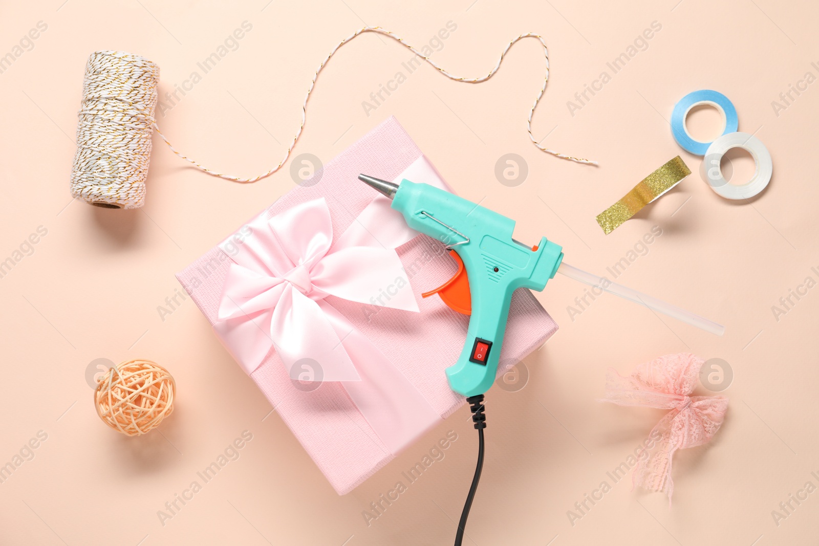 Photo of Hot glue gun, gift box and handicraft materials on pink background, flat lay