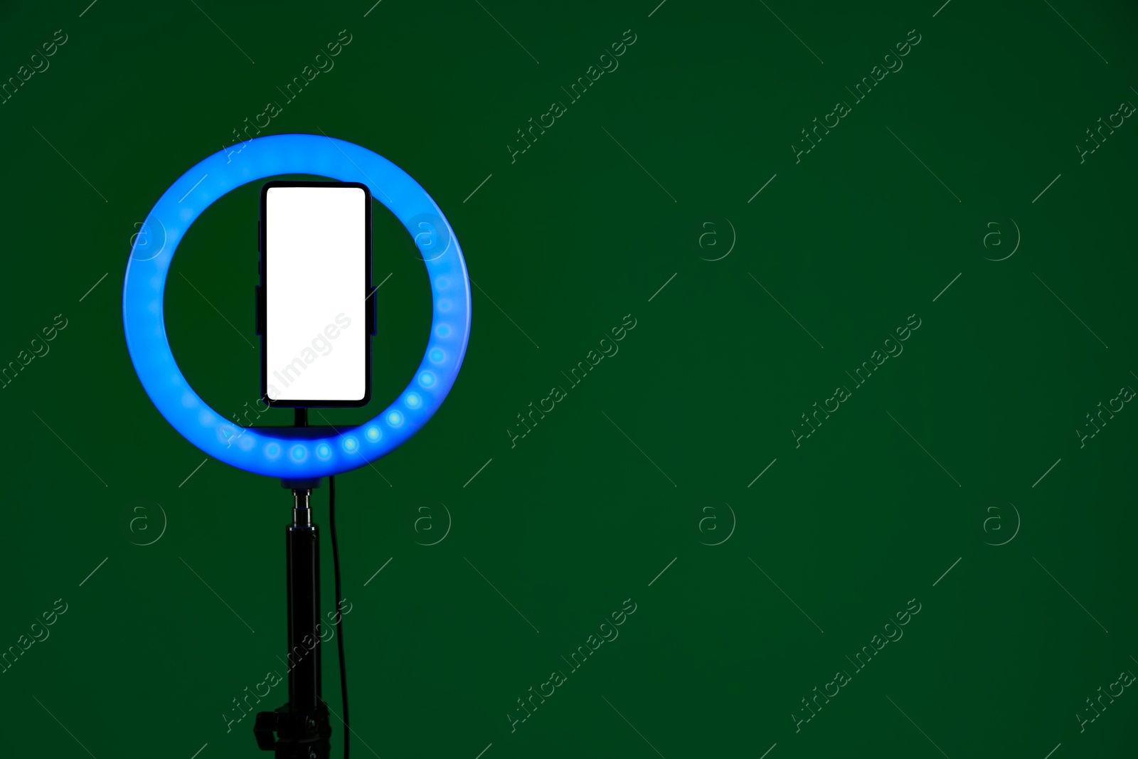 Photo of Ring lamp with smartphone on green background, space for text