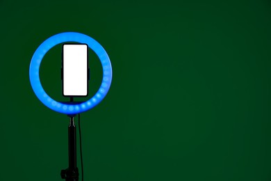 Photo of Ring lamp with smartphone on green background, space for text