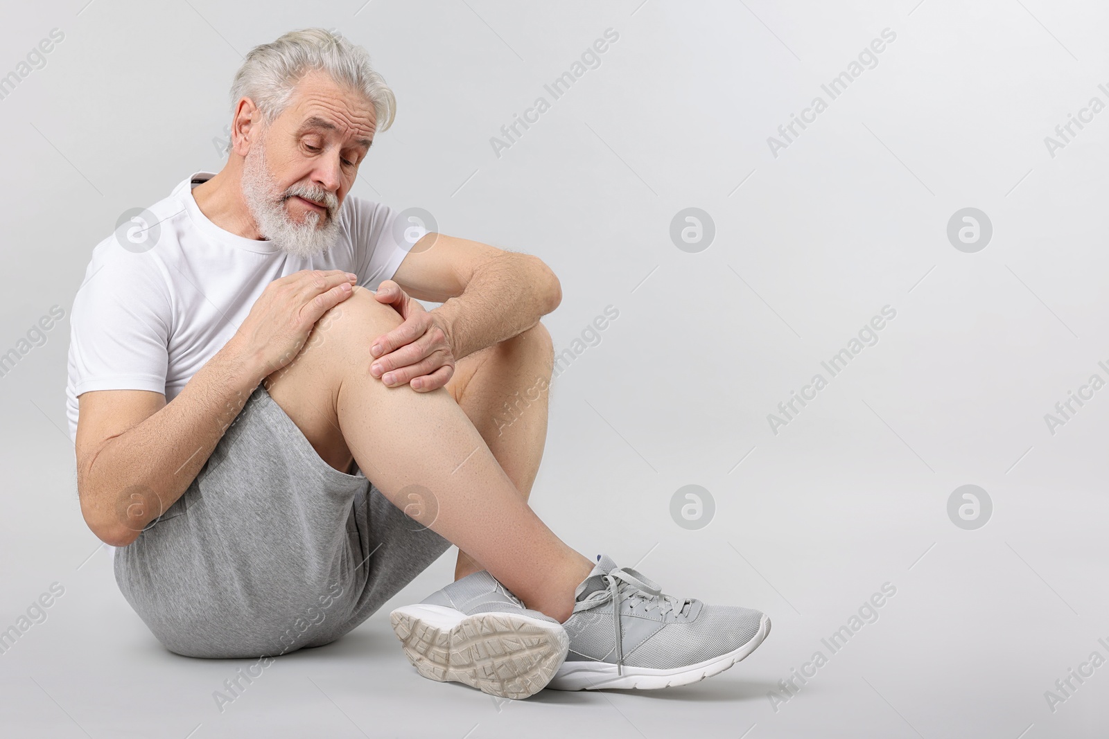 Photo of Senior man suffering from pain in his knee on light background. Space for text