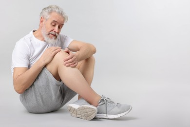 Photo of Senior man suffering from pain in his knee on light background. Space for text