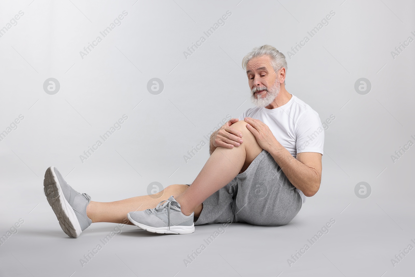 Photo of Senior man suffering from pain in his knee on light background