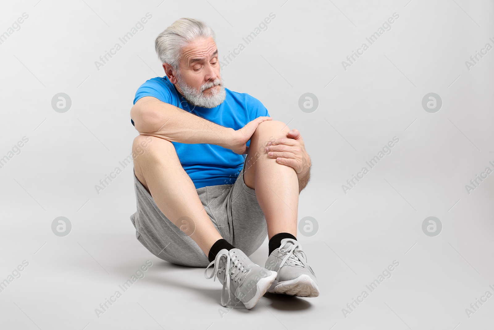 Photo of Senior man suffering from knee pain on light grey background