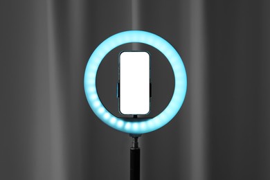 Photo of Glowing ring lamp with smartphone near black curtain