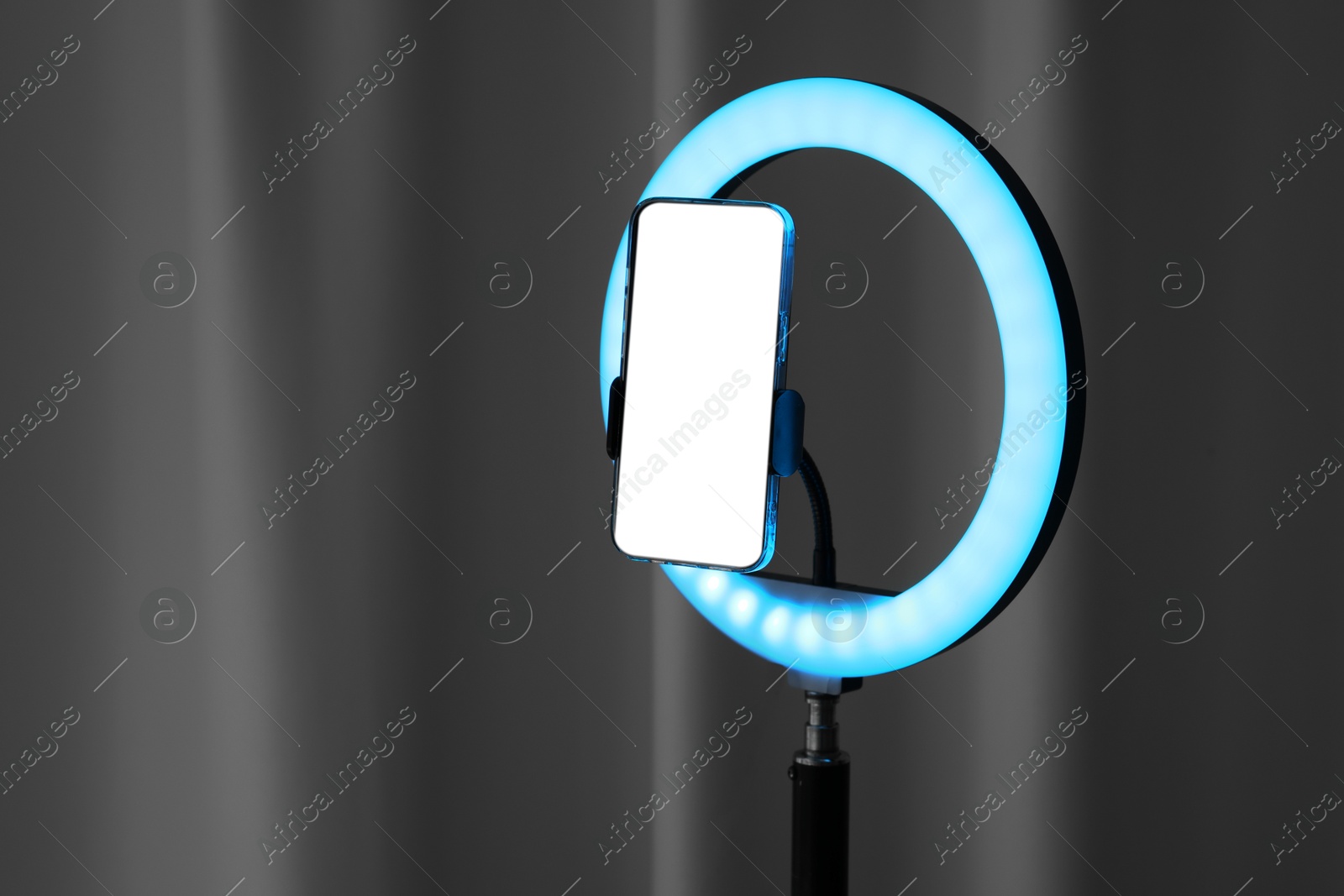 Photo of Glowing ring lamp with smartphone near black curtain. Space for text