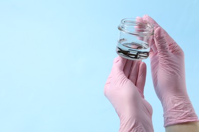 Photo of Woman holding glass jar with medicinal leeches on light blue background, closeup. Space for text