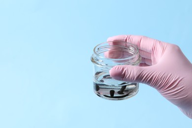 Photo of Woman holding glass jar with medicinal leeches on light blue background, closeup. Space for text