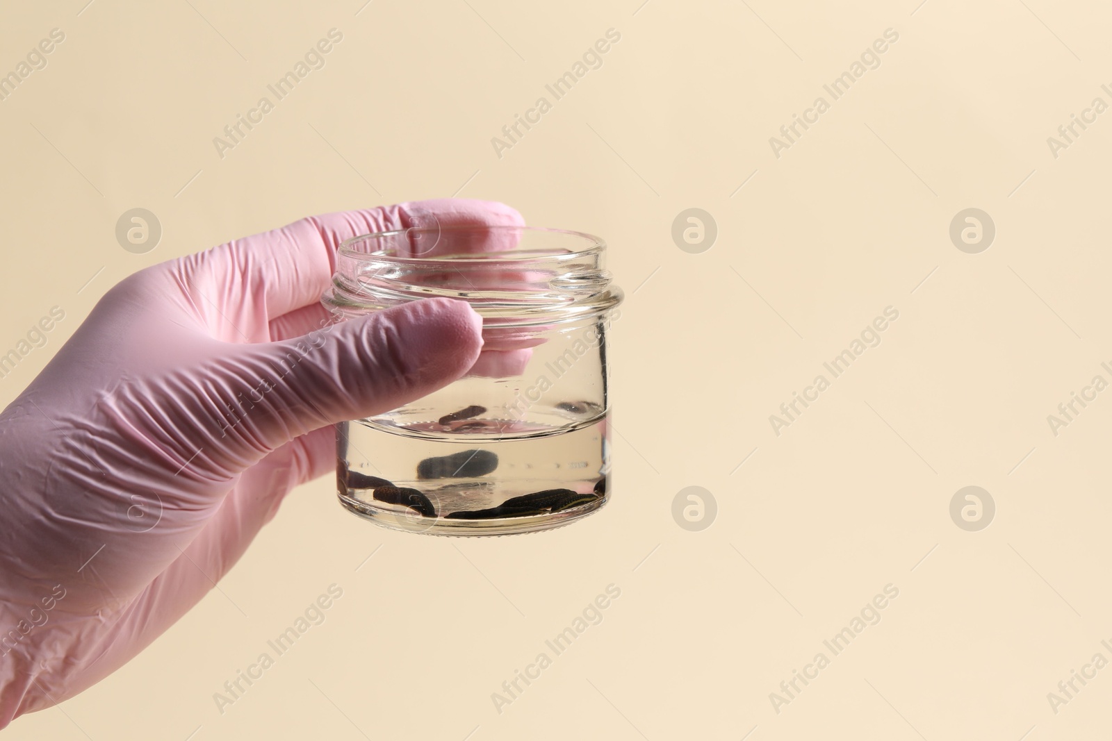 Photo of Woman holding glass jar with medicinal leeches on pale yellow background, closeup. Space for text