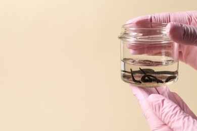 Photo of Woman holding glass jar with medicinal leeches on pale yellow background, closeup. Space for text