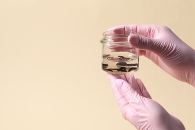 Photo of Woman holding glass jar with medicinal leeches on pale yellow background, closeup. Space for text