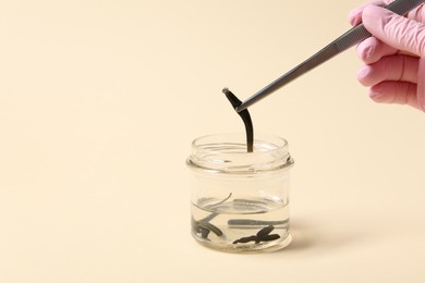 Photo of Woman taking medicinal leech from jar with tweezers on pale yellow background, closeup