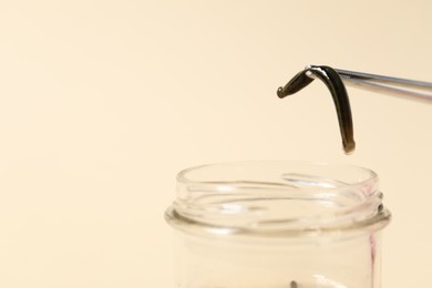 Photo of Taking medicinal leech from jar with tweezers on pale yellow background, closeup. Space for text