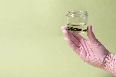 Photo of Woman holding glass jar with medicinal leeches on light green background, closeup. Space for text