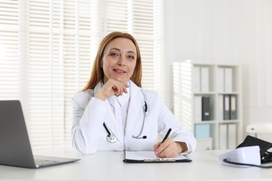 Cardiologist with stethoscope at white table in clinic