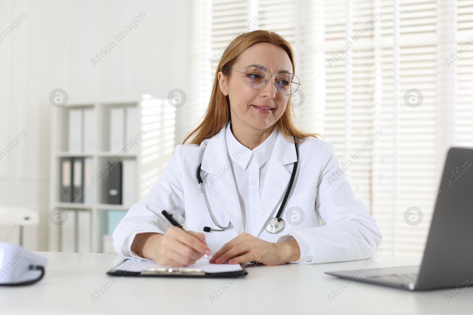 Photo of Cardiologist with stethoscope working at white table in clinic