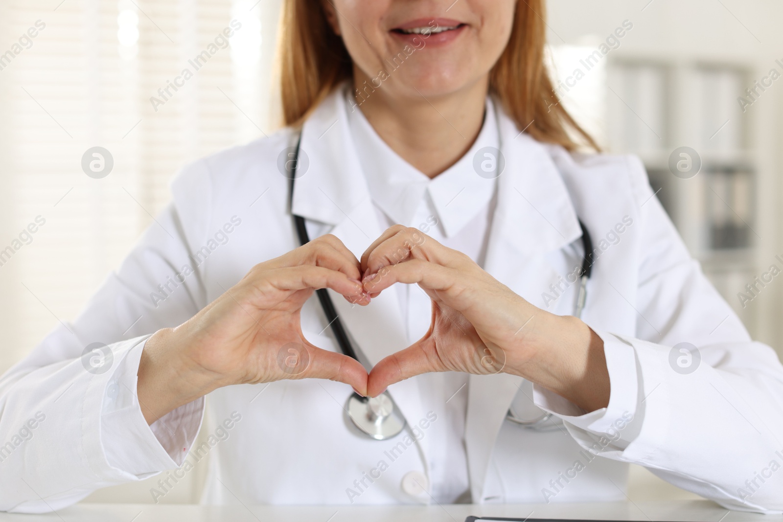 Photo of Cardiologist making heart with hands in hospital, closeup