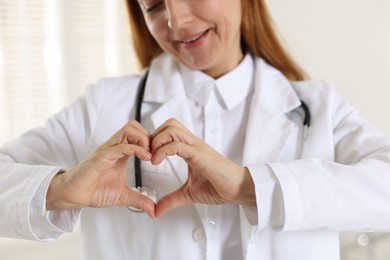 Photo of Cardiologist making heart with hands indoors, closeup