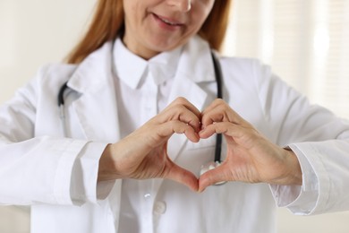 Photo of Cardiologist making heart with hands indoors, closeup