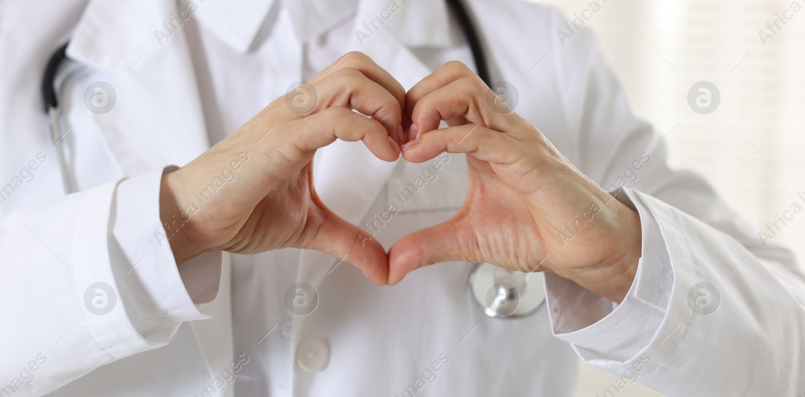 Photo of Cardiologist making heart with hands indoors, closeup