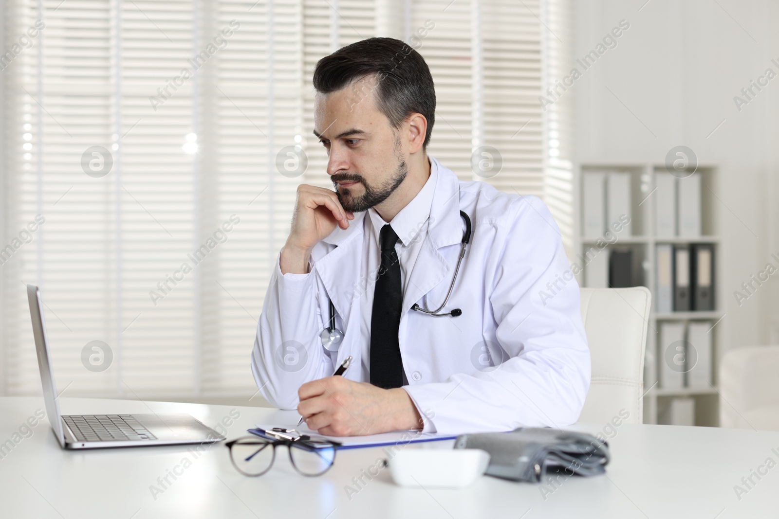 Photo of Cardiologist with stethoscope working at white table in clinic