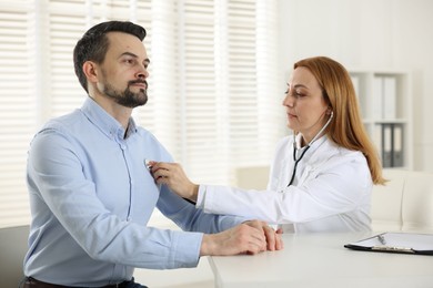 Photo of Cardiologist with stethoscope listening patient's heartbeat at desk in hospital